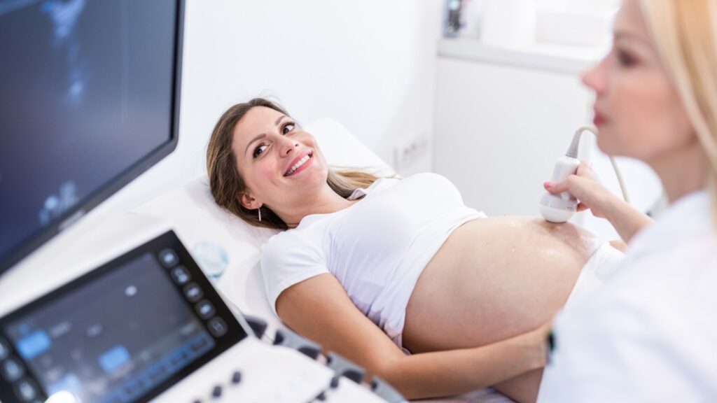 Patiente enceinte allongée lors d’une échographie à la clinique de fertilité, montrant le suivi médical de la grossesse avec un professionnel effectuant l’examen ultrasonore.