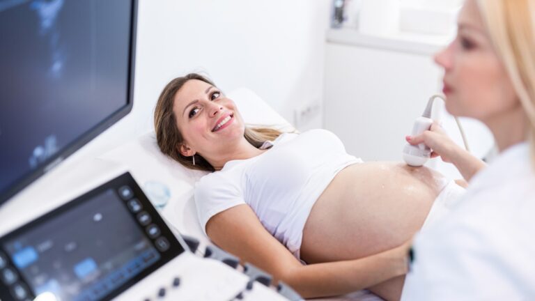 Patiente enceinte allongée lors d’une échographie à la clinique de fertilité, montrant le suivi médical de la grossesse avec un professionnel effectuant l’examen ultrasonore.