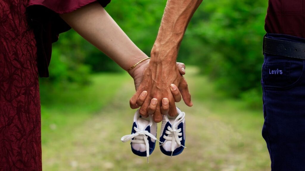 Un couple se tient la main et tient une paire de chaussons de bébé, symbole du désir d’enfant après un don d’ovocytes et une FIV en Grèce﻿