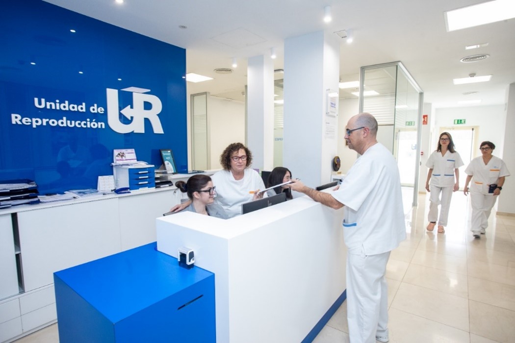 Le personnel de la clinique In Vitro travaillant dans la réception de la clinique UR Vistahermosa. Médecins, embryologistes et coordinatrices des patients en blouses blanches. Intérieur blanc avec des éléments de finition bleus. Inscription « Unidad de Reproduccion » sur le mur de la réception.