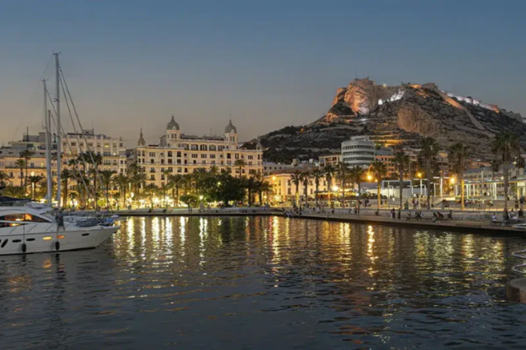 La marina d'Alicante, en Espagne, au crépuscule. Un ciel sans nuages, le soleil couchant et la lumière jaune des lampadaires.
